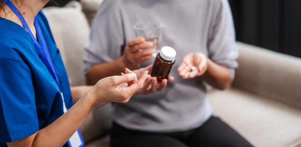Caucasian female doctor provides a glass of water and medication pills to an elderly Asian